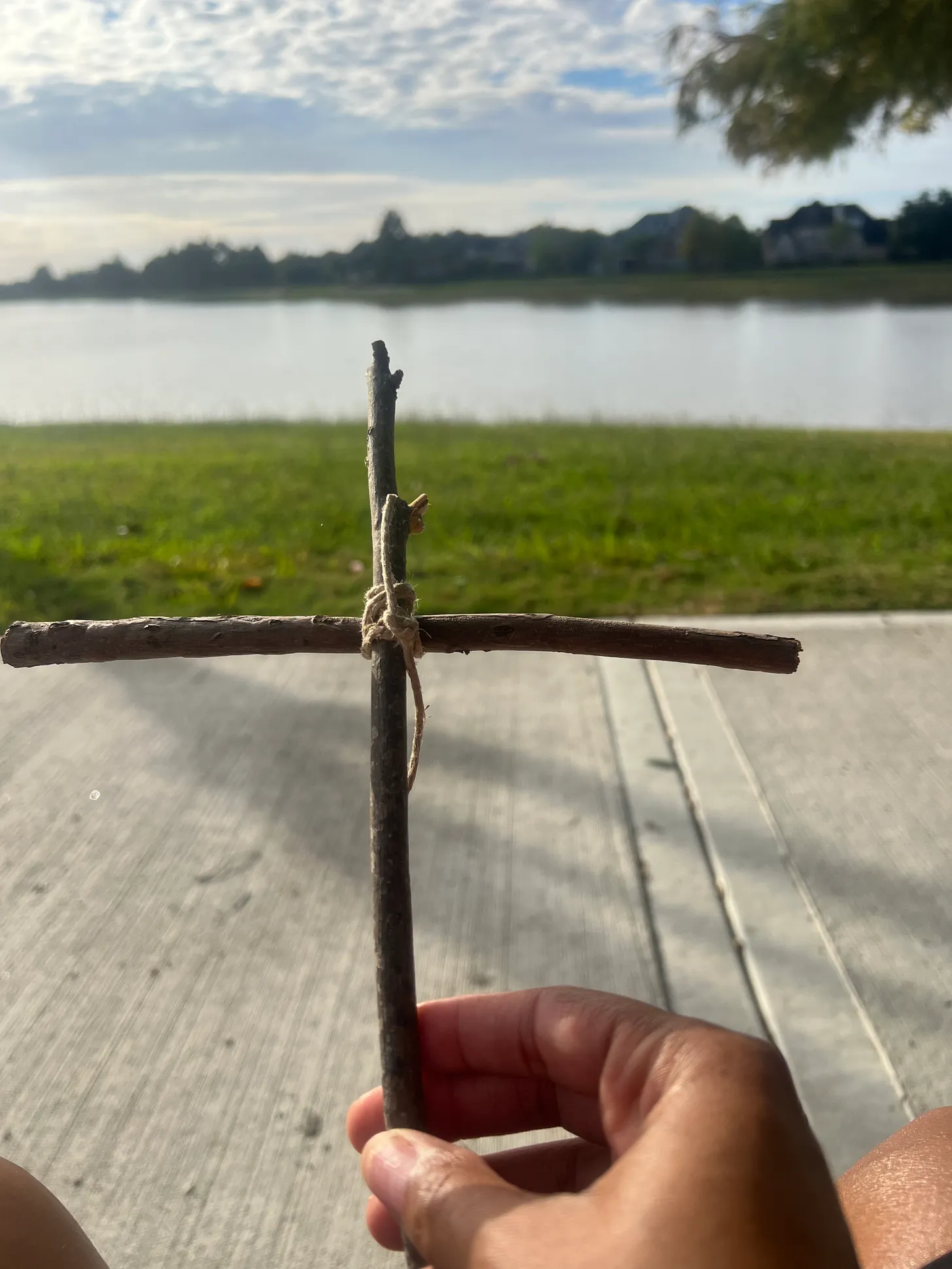 Holding a sticks shaped like a cross in front of a man made lake.